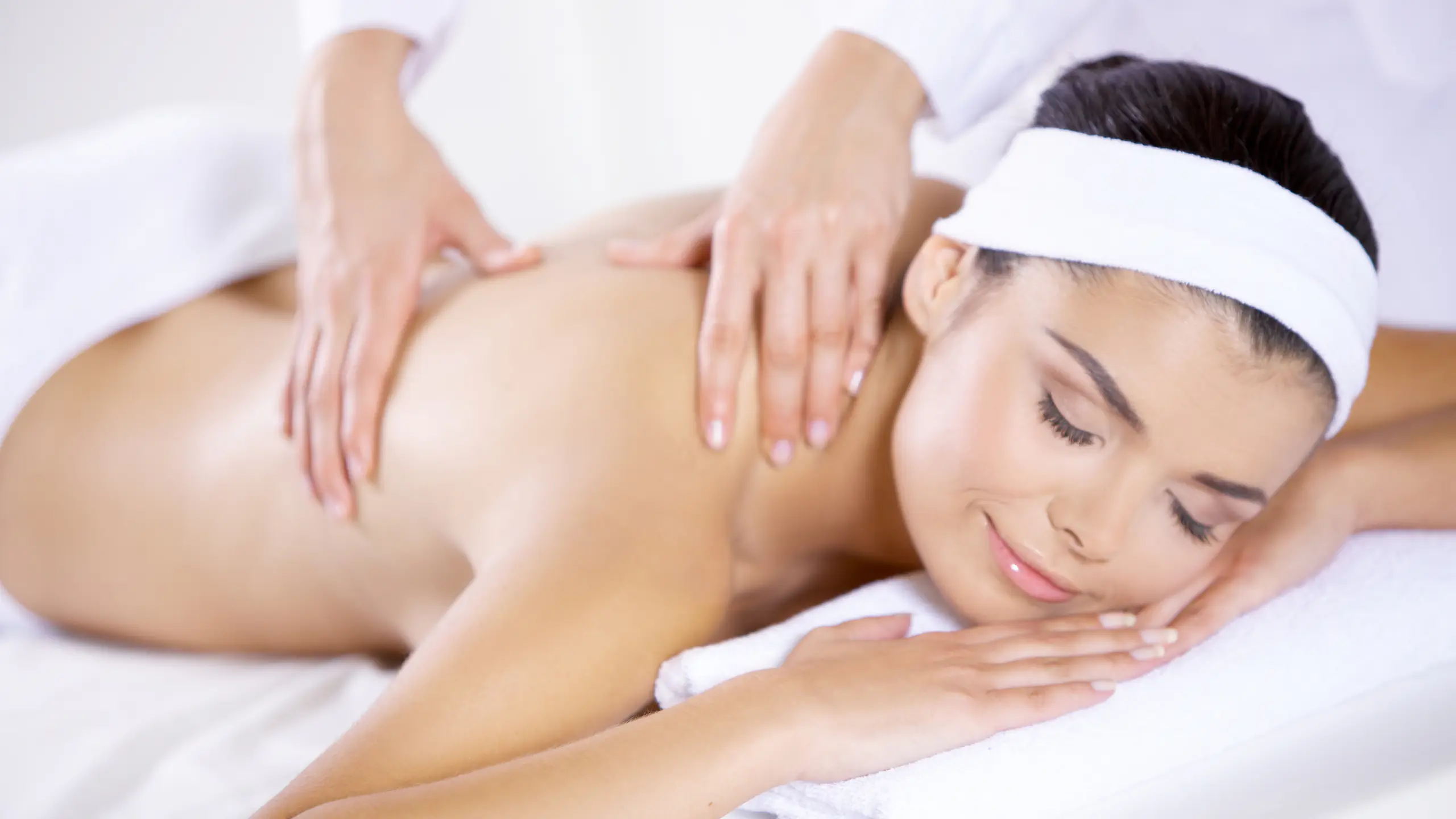 Wellness Mórahalom - Mosolygó nő háti masszázst kap fehér törölközőn.